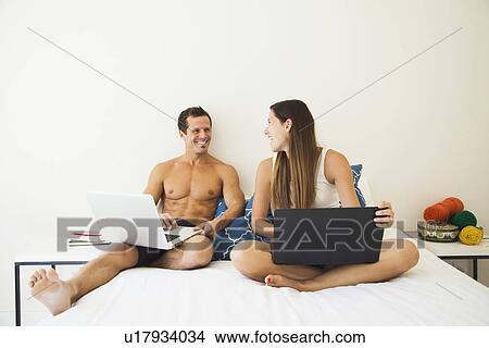 Couple lying on bed with laptop View Large Photo Image Picture - Couple lying on bed with laptop. Fotosearch