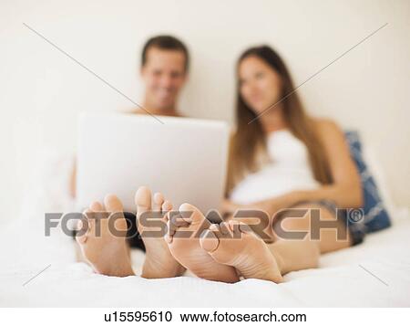 Couple lying on bed with laptop View Large Photo Image Stock Image - Couple lying on bed with laptop. Fotosearch