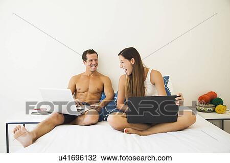 Couple lying on bed with laptop View Large Photo Image Stock Image - Couple lying on bed with laptop. Fotosearch