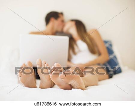 Couple lying on bed with laptop View Large Photo Image Stock Photograph - Couple lying on bed with laptop. Fotosearch