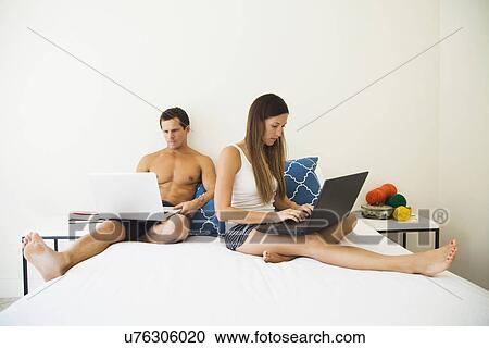 Couple lying on bed with laptops View Large Photo Image Stock Image - Couple lying on bed with laptops. Fotosearch