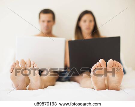 Couple lying on bed with laptops View Large Photo Image Stock Image - Couple lying on bed with laptops. Fotosearch