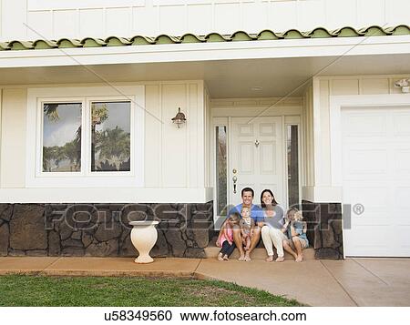 Stock Image - Family with three kids (6-7, 2-3, 6-11 months) sitting in front of house. Fotosearch