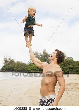 Stock Image - Father with son (6-11 months) on beach. Fotosearch