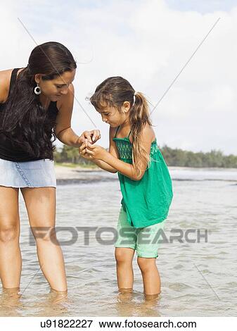 Stock Photo - Girl (6-7) with mother walking in sea. Fotosearch