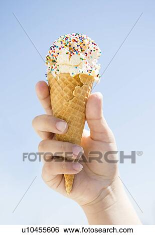 Stock Photograph - Girl (8-9) holding ice cream against blue sky. Fotosearch