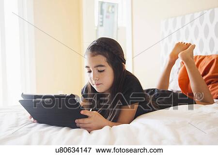Girl (8-9) laying on bed and using digital tablet View Large Photo Image Stock Photo - Girl (8-9) laying on bed and using digital tablet. Fotosearch