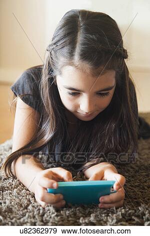 Stock Photo - Girl (8-9) playing mobile phone game. Fotosearch