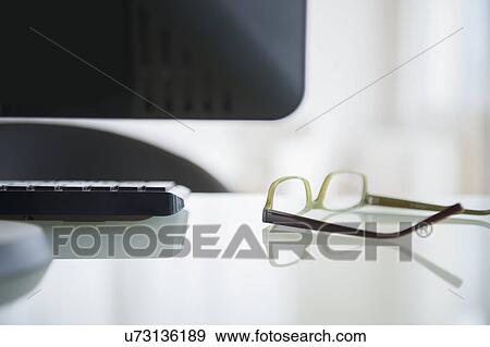 Stock Photo - Glasses lying on desk near computer, studio shot. Fotosearch