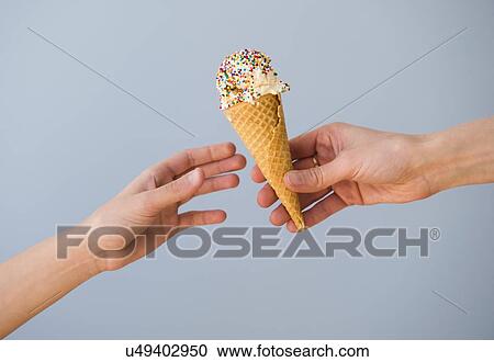 Stock Image - Hands passing ice cream against blue sky. Fotosearch