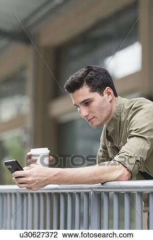 Stock Image - Man drinking coffee and text messaging. Fotosearch