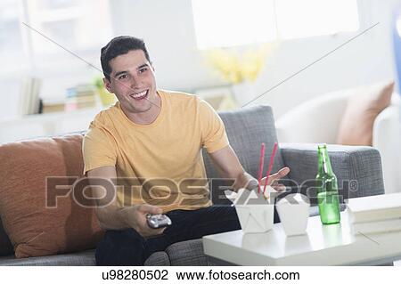 Stock Image - Man eating take out meal and watching television. Fotosearch