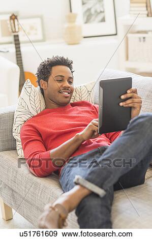 Man lying on sofa and using tablet PC View Large Photo Image Stock Photo - Man lying on sofa and using tablet PC. Fotosearch