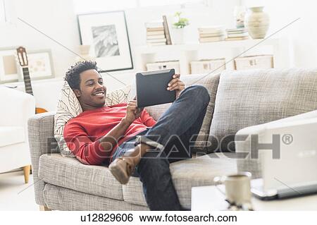 Man lying on sofa and using tablet PC View Large Photo Image Stock Photograph - Man lying on sofa and using tablet PC. Fotosearch