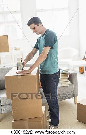 Stock Image - Man packing cardboard boxes at home. Fotosearch