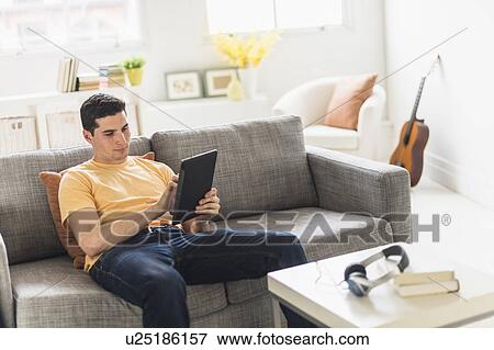 Man sitting on sofa and using digital tablet View Large Photo Image Stock Photo - Man sitting on sofa and using digital tablet. Fotosearch