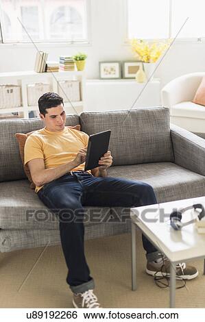 Man sitting on sofa and using digital tablet View Large Photo Image Stock Photograph - Man sitting on sofa and using digital tablet. Fotosearch