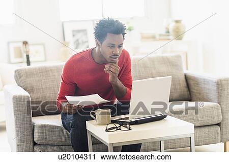 Stock Image - Man sitting on sofa and using laptop. Fotosearch