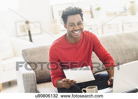 Stock Image - Man sitting on sofa and using laptop. Fotosearch
