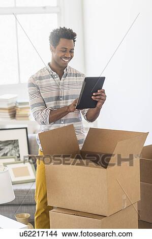 Picture - Man using tablet PC while unpacking cardboard box. Fotosearch