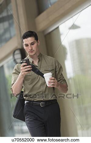 Stock Image - Man walking on street and text messaging. Fotosearch