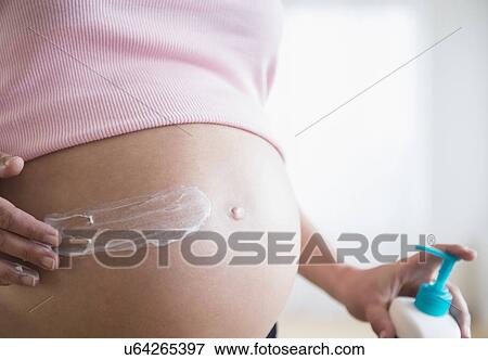 Stock Photo - Mid section of pregnant woman applying moisturizer on her belly. Fotosearch