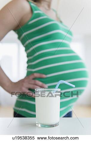 Stock Photography - Mid section of pregnant woman, glass of milk in front. Fotosearch