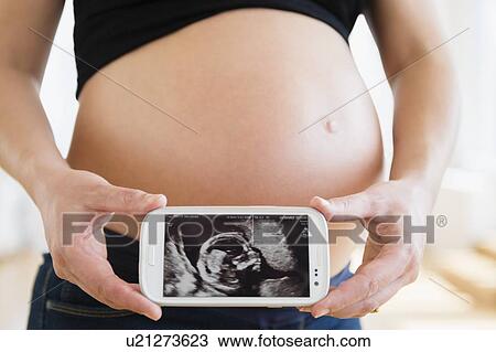 Stock Image - Mid section of pregnant woman holding mobile phone. Fotosearch