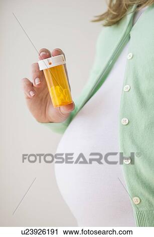 Stock Image - Mid section of pregnant woman holding pill bottle. Fotosearch