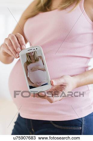 Stock Image - Mid section of pregnant woman holding mobile phone. Fotosearch