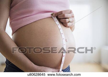 Stock Photography - Mid section of pregnant woman measuring her belly. Fotosearch