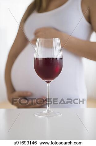 Stock Photograph - Mid section of pregnant woman, red wine in front. Fotosearch