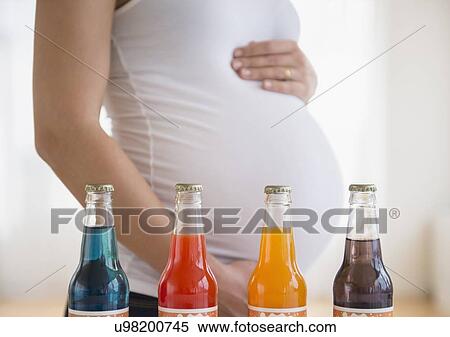 Stock Photography - Mid section of pregnant woman, soda bottles in front. Fotosearch