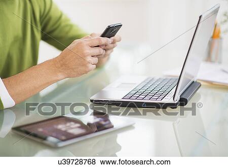 Stock Photo - Mis section of man using mobile phone at desk. Fotosearch