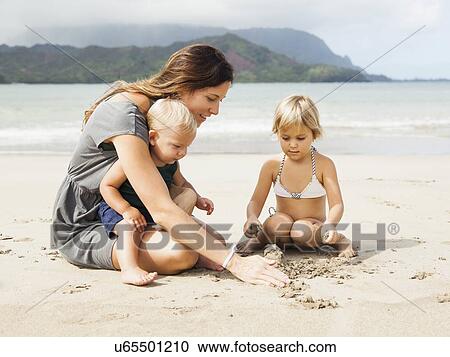 Stock Image - Mother playing with daughters (6-11 months, 2-3) on beach. Fotosearch