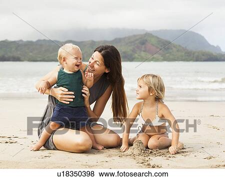 Stock Photo - Mother playing with daughters (6-11 months, 2-3) on beach. Fotosearch