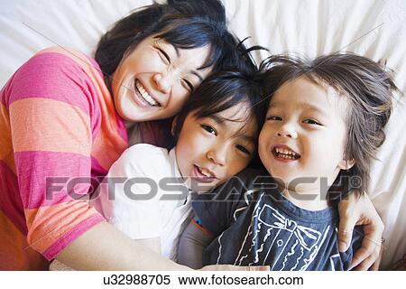 Stock Photography - Mother with children cuddling on bed. Fotosearch