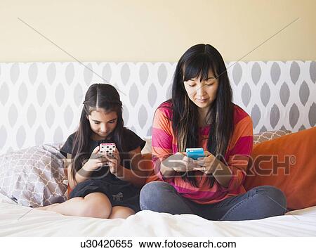 Stock Photography - Mother with daughter (8-9) sitting and using cell phones. Fotosearch