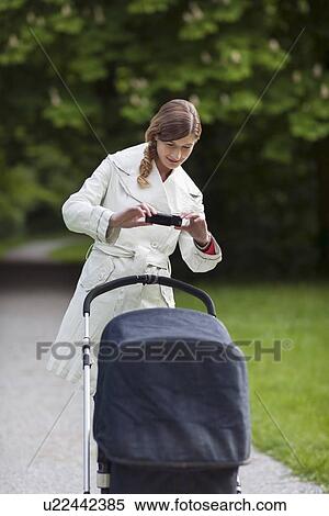 Stock Photography - Mother with pram in park taking picture with cell phone. Fotosearch