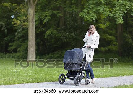 Stock Image - Mother with pram in park talking on mobile phone. Fotosearch