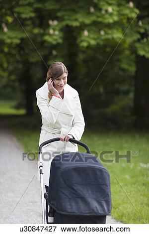 Stock Photo - Mother with pram in park talking on mobile phone. Fotosearch