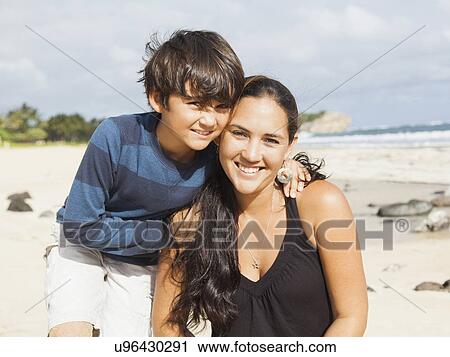Stock Image - Portrait of boy (10-11) sitting on beach with mother. Fotosearch