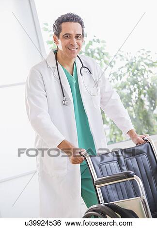 Stock Photograph - Portrait of doctor standing by wheelchair. Fotosearch