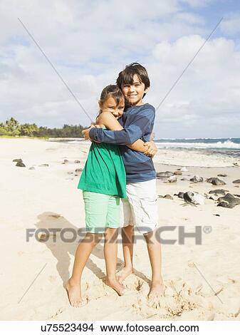 Picture - Portrait of girl (6-7) and boy (10-11) embracing on beach. Fotosearch