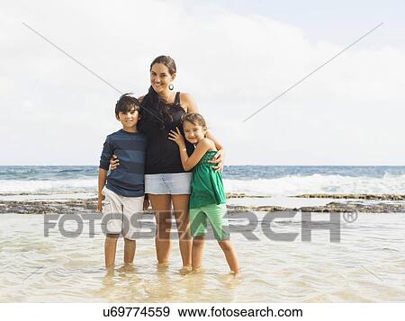 Stock Photo - Portrait of girl (6-7) and boy (10-11) standing on beach with mother. Fotosearch