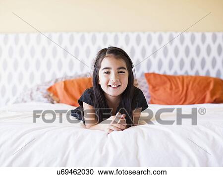 Stock Image - Portrait of girl (8-9) laying on bed. Fotosearch