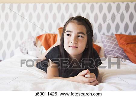 Stock Photography - Portrait of girl (8-9) laying on bed. Fotosearch