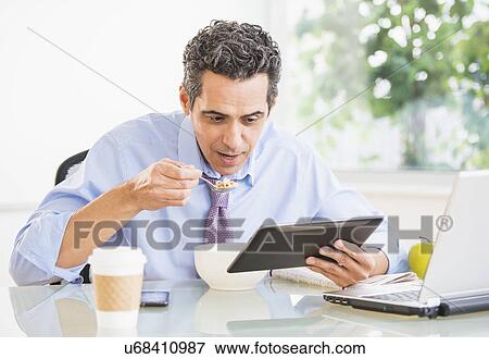 Portrait of man eating and using digital tablet View Large Photo Image Stock Photo - Portrait of man eating and using digital tablet. Fotosearch