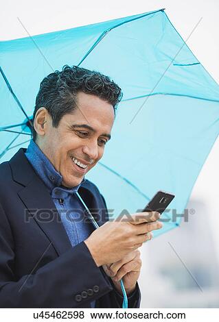 Portrait of man holding blue umbrella and using mobile phone View Large Photo Image Stock Photo - Portrait of man holding blue umbrella and using mobile phone. Fotosearch