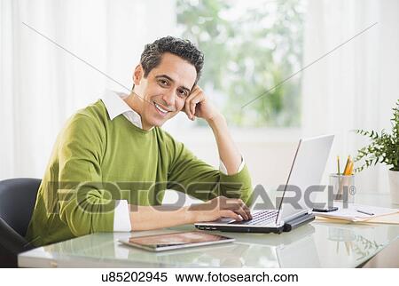 Stock Photography - Portrait of man working on laptop at home. Fotosearch